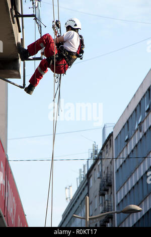 Belgrad, Serbien - November 19, 2018: industriekletterer am Seil hängend während der Installation von Werbebanner auf einer Bilding, Low Angle View Stockfoto