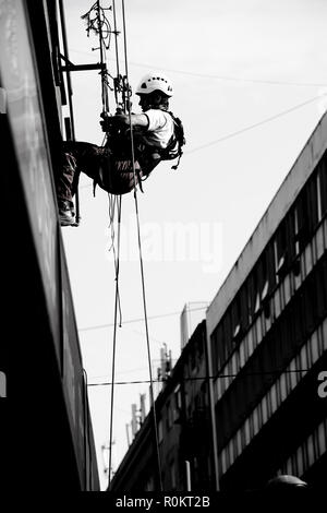 Belgrad, Serbien - November 19, 2018: industriekletterer am Seil hängend während der Installation von Werbebanner auf einer Bilding, Low Angle View in blac Stockfoto