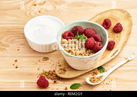 Hausgemachtes Müsli und Joghurt in eine Schüssel geben und mit Himbeeren auf einen hölzernen Tisch. Stockfoto