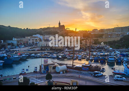 GHAJNSIELEM, MALTA - 15. Juni 2018: Die feurigen Sonnenuntergang über dem Hafen von Mgarr mit der Silhouette von Lourdes Kapelle auf Hintergrund, am 15. Juni in Ghajnsi Stockfoto