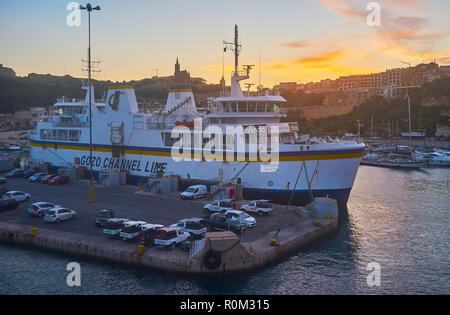 GHAJNSIELEM, MALTA - 15. JUNI 2018: abends Abfahrt von der Fähre mit Blick auf Hafen von Mgarr, Silhouette der Pfarrkirche auf dem Hil Stockfoto