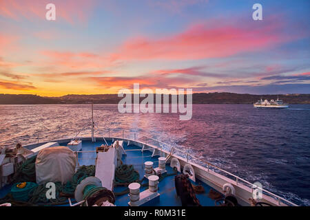 Der Blick auf die Fähre, Floating auf der Insel Gozo aus Malta auf Twilight mit hellen Feurigen Wolken im Himmel. Stockfoto