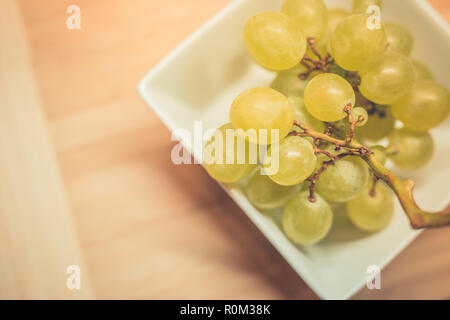 Bunch of green grapes in the basket, fruits of autumn, a symbol of abundance on rustic wood background with copy space, top view, close-up. Stockfoto