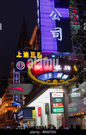 Beleuchtete vertikale und hängende Ladenschilder leuchten nachts auf der Nanjing Road, Shanghai, China, über Bürgersteig und Ladenfronten Stockfoto