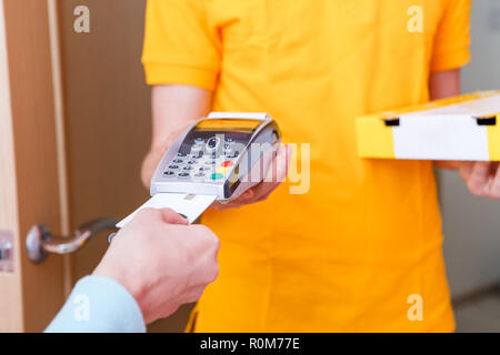 Foto von Kurier in gelben T-Shirt mit Box mit Pizza und Point-of-Sale Stockfoto