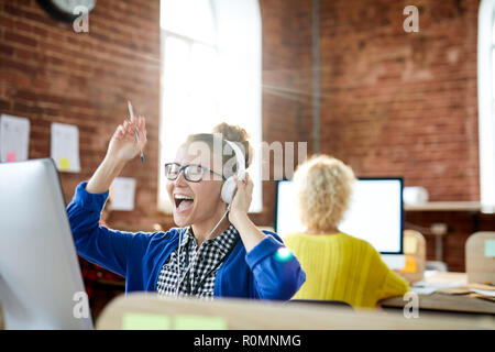 Junge aufgeregt Frau in casualwear Hören von Musik über Kopfhörer und Video Clip auf Bildschirm Stockfoto