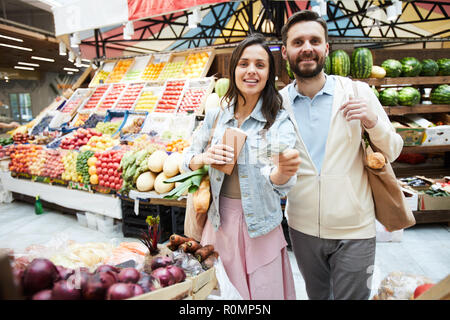 Positive schöne junge Paar in Freizeitkleidung bei Farmers Market und Kamera, Geld für den Kauf Stockfoto