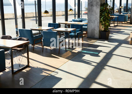 Holztische und blauen Stühlen entlang Windows im Cafe von Riverside an einem sonnigen Tag Stockfoto