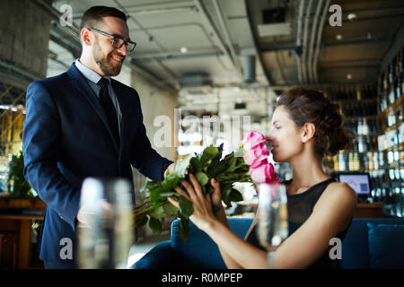 Glückliche junge Frau riecht Bündel Rosen von ihrem Freund im Restaurant Stockfoto