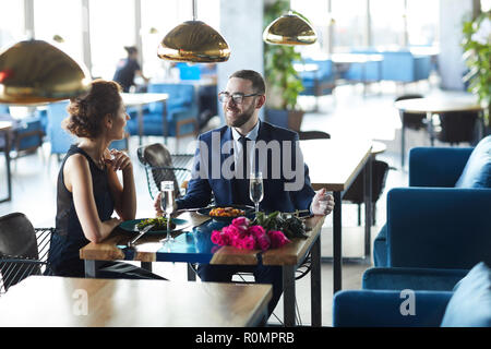 Junge elegantes Paar sitzt von Tisch im Restaurant, im Gespräch und in Champagner und Mittagessen Stockfoto
