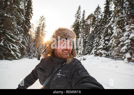 Happy kaukasischen Mann in einer Pelzmütze genießen Sie den verschneiten Winterwald. Stockfoto