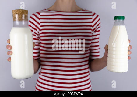 Null Abfall Konzept. Schöne Frauen Halten in der Hand ein Glas wiederverwendbare Flasche Milch und in der anderen Hand Plastikflasche. Stockfoto