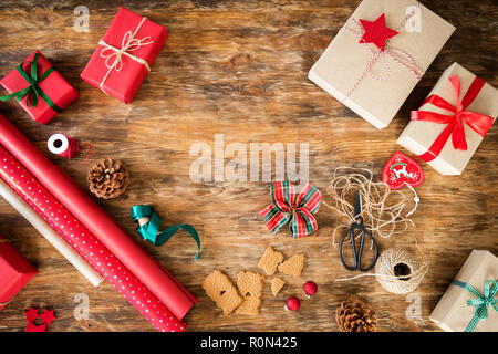 DIY Geschenkverpackung. Schöne rote Weihnachtsgeschenke auf rustikalen Holztisch. Blick von oben auf die Weihnachten folierstation. Stockfoto