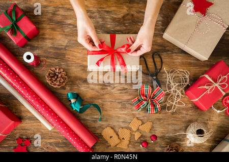 DIY Geschenkverpackung. Frau Verpackung schöne Weihnachtsgeschenke auf rustikalen Holztisch. Ansicht von Weihnachten folierstation. Stockfoto