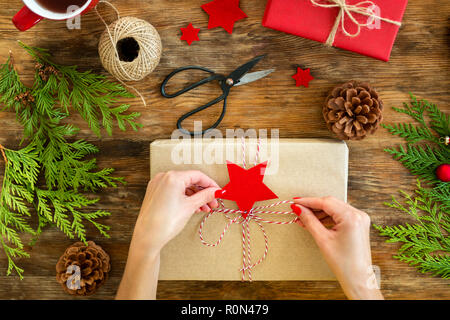 DIY Geschenkverpackung. Frau Verpackung schöne rote Weihnachtsgeschenke auf rustikalen Holztisch. Overhead Sicht von Weihnachten folierstation. Stockfoto