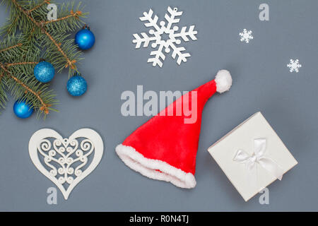 Weihnachtsdekoration. Geschenkbox, Santa's Hut, Tannenbaum Äste mit Spielzeug Bälle auf grauem Hintergrund. Ansicht von oben. Weihnachten Grußkarten-Konzept. Stockfoto