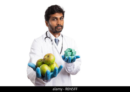 Indische männlichen Ernährungsberater oder Medic Holding grüne Äpfel in einer Hand und Maßband in der Anderen als gesunden Lebensstil Konzept isoliert auf weißem Stockfoto