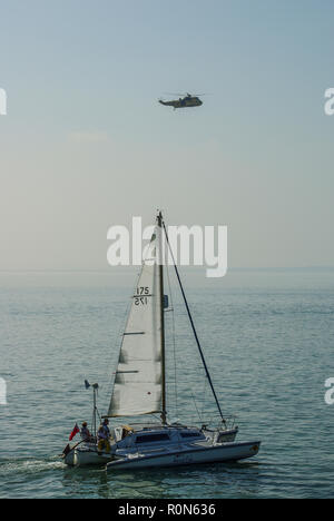 RAF Sea King Air Sea Rescue Hubschrauber über einem nebligen Meer mit einer Yacht segeln im Vordergrund fliegen. Thames Estuary in Southend On Sea, Essex, Großbritannien Stockfoto