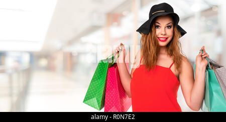Attraktive, junge Frau im roten Kleid hält Taschen in den Händen und genießt, Shopping in der Mall (Kopie) Stockfoto