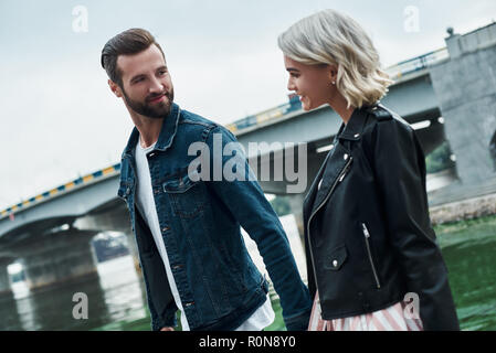 Romantisches date im Freien. Junges Paar zu Fuß auf der Straße in der Nähe von Wasser, Hände halten sich einander reden Lächeln freudigen close-up Stockfoto
