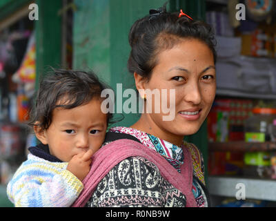 Jungen nordöstlichen indischen Monpa Bergvolk Frau trägt Ihr Kleinkind Junge in einer traditionellen Babytragetuch auf ihrem Rücken. Stockfoto