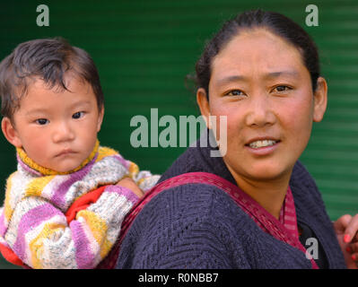 Junge indische Monpa Bergvolk Frau trägt Ihr Kleinkind Junge in einer traditionellen Babytragetuch auf ihrem Rücken. Stockfoto