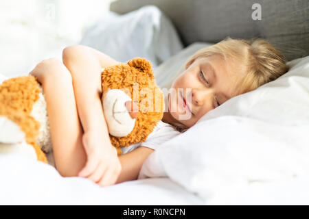 Ein kleines Mädchen im Bett schlafen und träumen mit Teddybär,