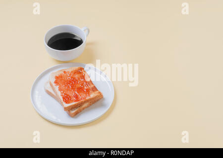 Zwei Scheiben Toast mit Erdbeermarmelade Gelee auf eine weiße Platte mit einer Tasse Kaffee auf einem Vintage tan Hintergrund mit Kopieren und Platz für Text Stockfoto