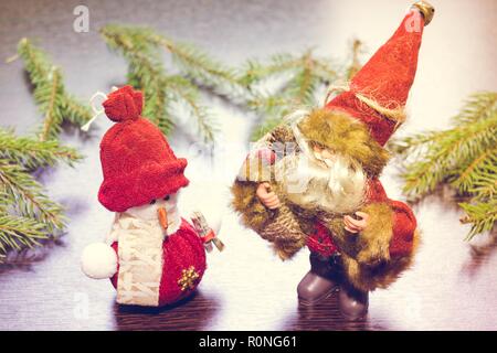 Santa Claus oder Der Weihnachtsmann steht neben einem neuen Jahr Schneemann auf einem hölzernen Hintergrund mit Tannenzweigen. Stockfoto