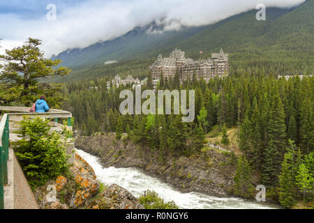 BANFF, AB, Kanada - Juni 2018: die Person auf dem Aussichtspunkt Anzeigen der Bow River Falls. In der Ferne ist das Fairmont Banff Springs Hotel. Stockfoto