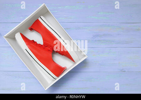 Rote Turnschuhe in der Box. Auf einem blauen Hintergrund aus Holz. Stockfoto