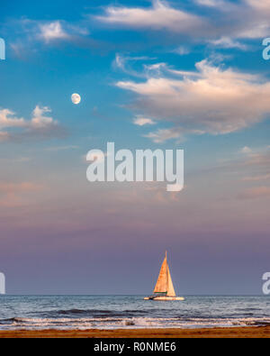 Ein Segelboot auf das Meer mit der fast volle Mond im Himmel oben, blau, pink und lila aus der Sonne Stockfoto