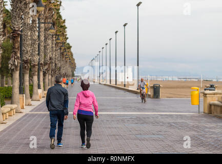 Nicht identifizierbare aktive Paare gehen auf eine Zement Beach Boardwalk von Palmen und Lampe Beiträge auf eine trübe, windigen Tag gefüttert Stockfoto