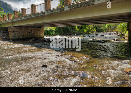 Schnell fließenden Fluss unter einer Brücke gehen mit der Sonne das Wasser und Felsen reflektieren Stockfoto