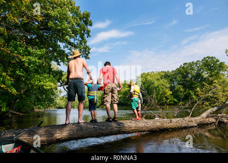 Zwei Männer und drei Kinder stehen auf einer gefallenen Baum Angeln, United States Stockfoto