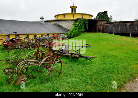 Alte landwirtschaftliche Geräte neben Scheunen und runde Scheune am Hancock Shaker Village Museum in der Nähe von Pittsfield MA, USA Stockfoto