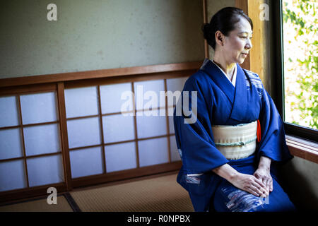 Japanische Frau, die traditionelle hellen blauen Kimono mit cremefarbenen Obi kniend auf dem Boden in der traditionellen japanischen Haus. Stockfoto