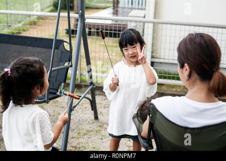 Zwei japanische Mädchen holding Würstchen am Spieß und Frau in einem Hinterhof. Stockfoto