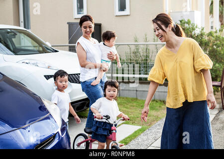 Zwei lächelnde Japanische Frauen und drei Kinder neben dem geparkten Auto in einer Straße. Stockfoto