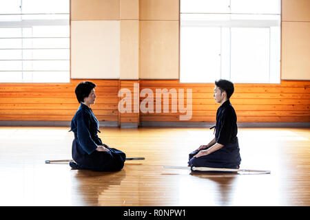 Weibliche und männliche Japanische Kendo Kämpfer kniete sich einander gegenüber auf Holzboden. Stockfoto