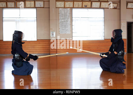 Zwei japanische Kendo Kämpfer sitzen einander gegenüber auf Holzboden, tragen Kendo Masken und Holding Holz Schwerter. Stockfoto