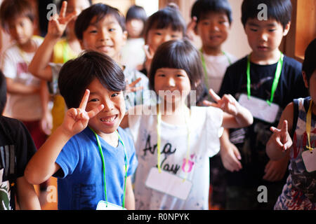 Gruppe von lächelnden Kinder in einer japanischen Vorschule, Frieden zu unterzeichnen, auf Kamera. Stockfoto