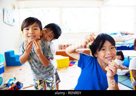 Drei junge Kinder in einer japanischen Vorschule, an der Kamera und Grimassen suchen, lächelnd. Stockfoto