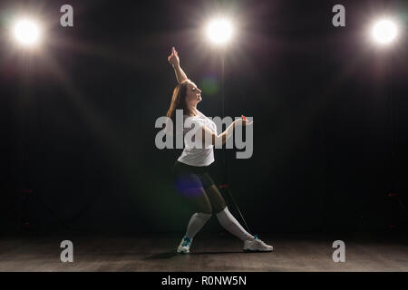 Dance, Hip Hop, Jazz Funk und Personen Konzept - flexible junge Frau tanzen in der Dunkelheit unter dem Licht Stockfoto