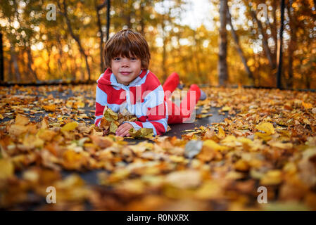 Porträt eines lächelnden Jungen liegen auf einem Trampolin im Herbst die Blätter fallen, United States Stockfoto