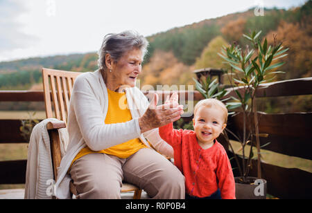 Ältere Frau mit einem Kleinkind Urenkel auf einer Terrasse im Herbst, die hohe fünf. Stockfoto