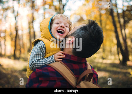 Eine ausgereifte Vater Holding ein Kleinkind Sohn in einem Herbst Wald, Spaß zu haben. Stockfoto