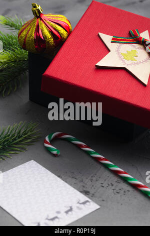 Tannenzweigen auf Beton Grau mit roter Geschenkbox und Dekorationen. Weihnachten und neues Jahr. Flach. Stockfoto
