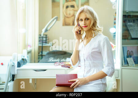 Eine junge Frau in einem weißen Gewand, in der die Telefonnummer im Büro von einer Kosmetikerin. Stockfoto