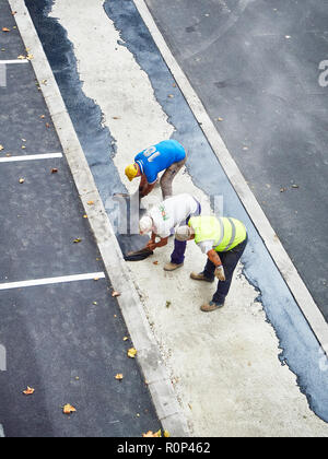 Arbeiter die manuelle Anwendung von frischem Asphalt während der Herstellung einer Fußgängerzone. Stockfoto